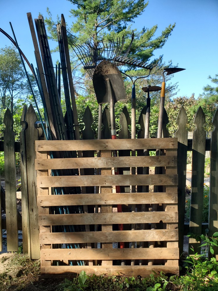 single wood pallet standing upright holding garden tools