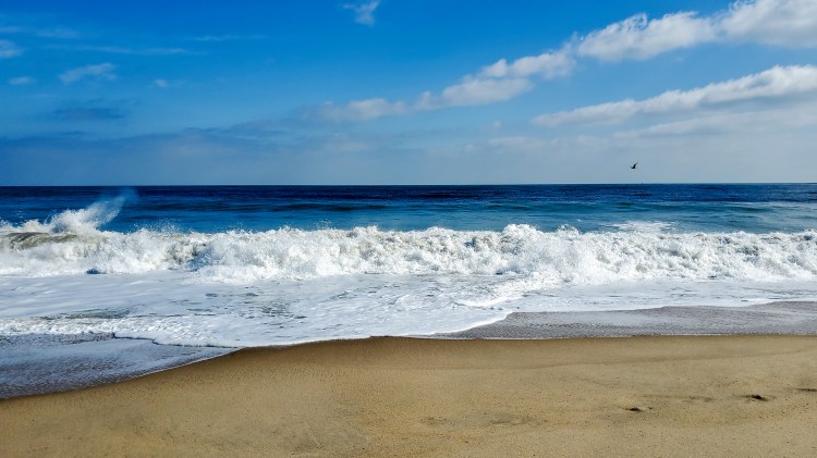 Waves crashing on the beach with blue skies